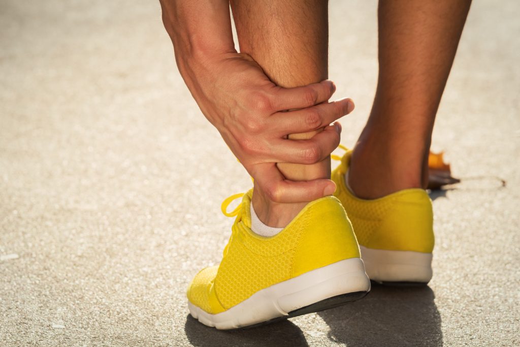 Man holds ankle that was sprained while jogging in yellow shoes.